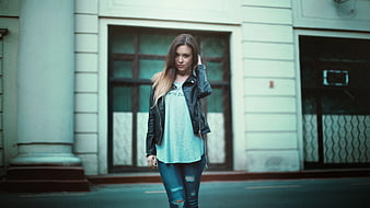 Young woman in leather jacket and ripped jeans standing on street