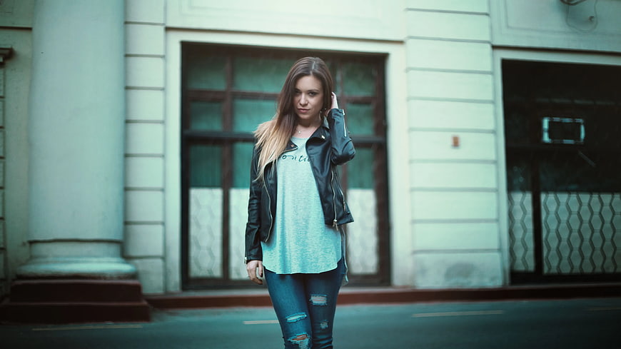 Young woman in leather jacket and ripped jeans standing on street