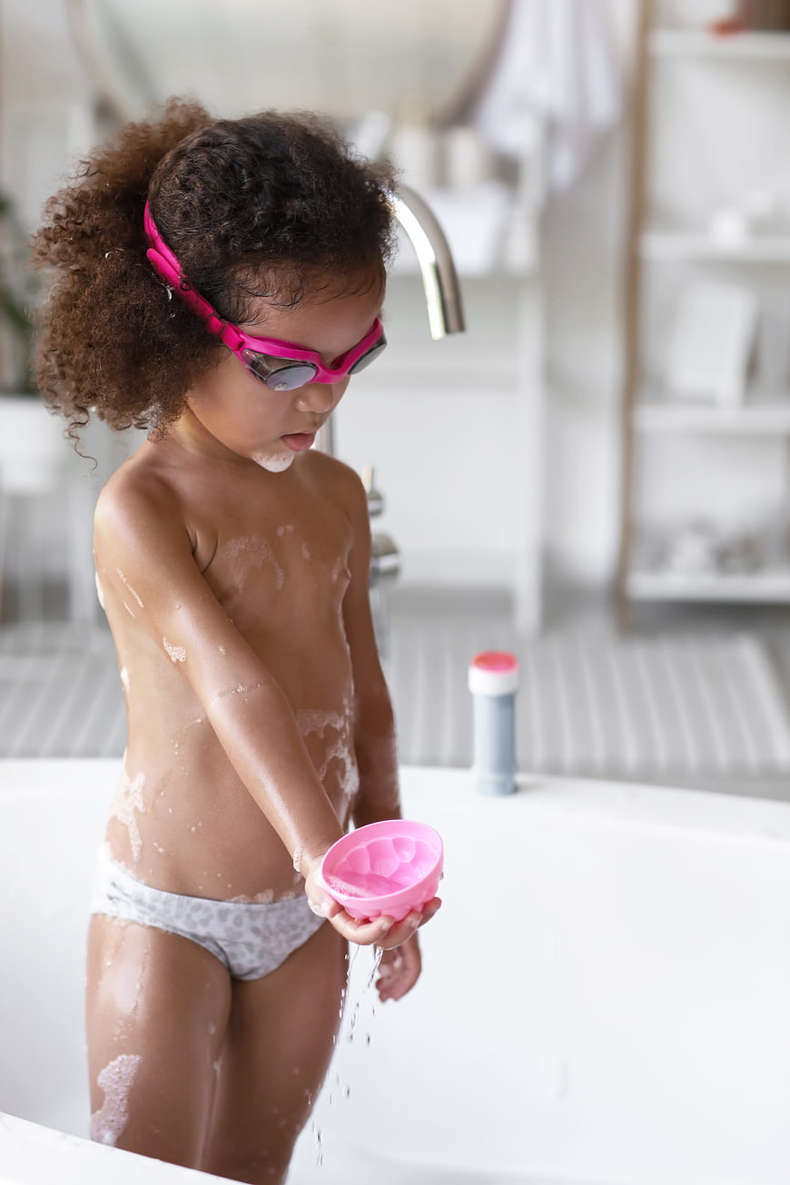 Cute little girl with pink goggles playing in a soapy bathtub