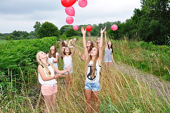 Teenage Girls Releasing Red Balloons in a Field