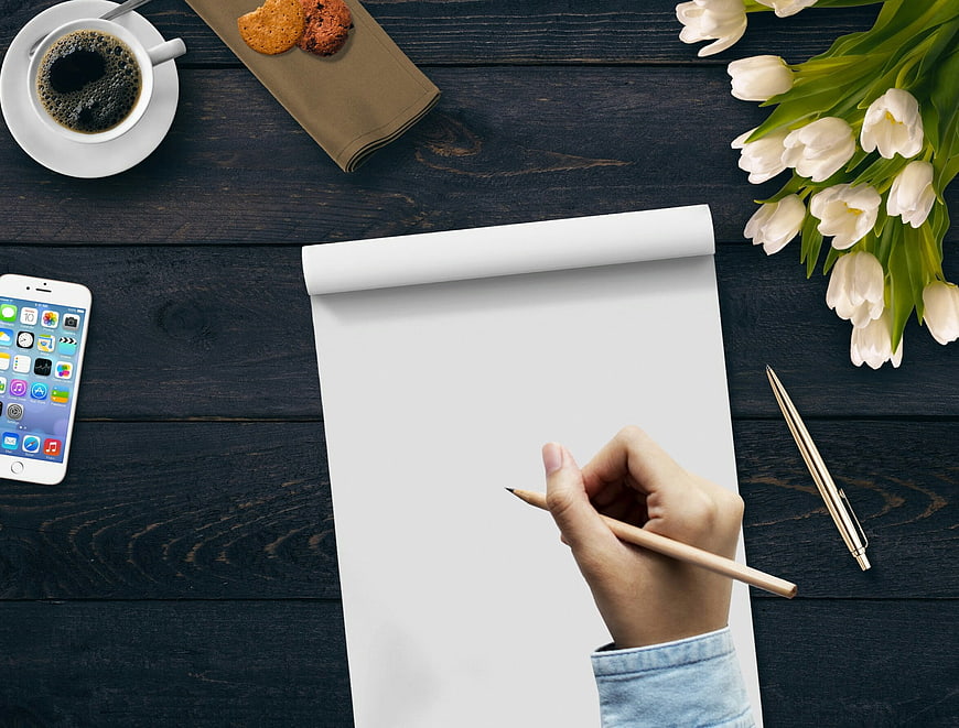 Hand Writing On Blank Paper With Coffee, Tulips, And Smartphone On Dark Wood