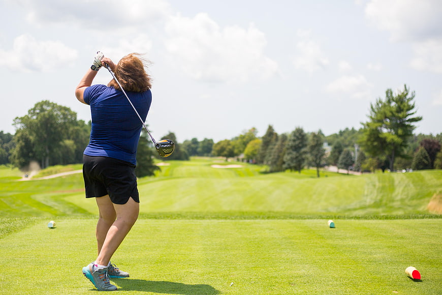 Woman Golfer Swinging Club on Green Course