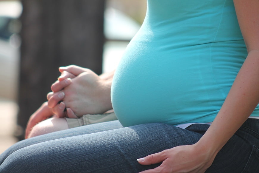 Pregnant woman in teal top holding hands with partner outdoors