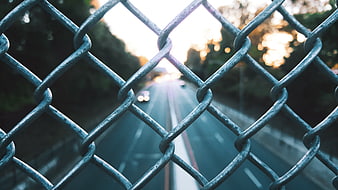 Chain link fence view of blurred road at sunset