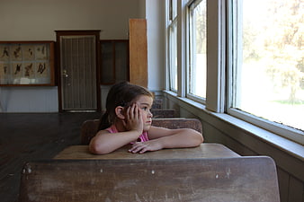 Young girl daydreaming at a vintage wooden school desk