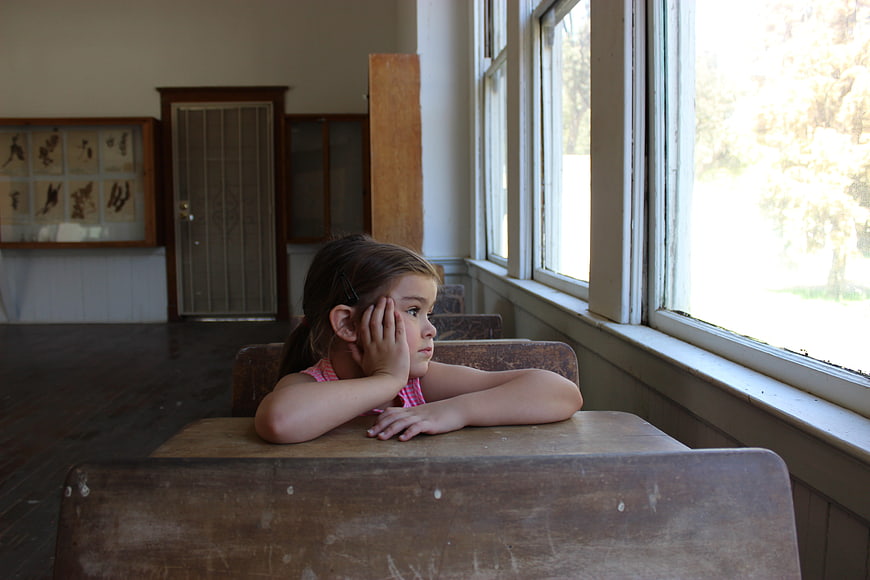 Young girl daydreaming at a vintage wooden school desk