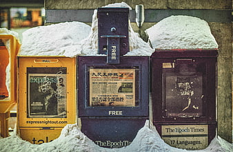 Snow-covered newspaper vending boxes on a city street
