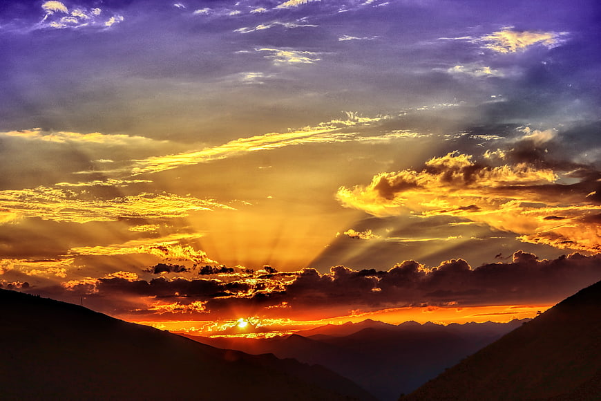 Dramatic Sunset Over Mountain Silhouettes with Golden Sunbeams