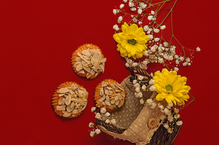 Almond cookies and yellow flowers on red background