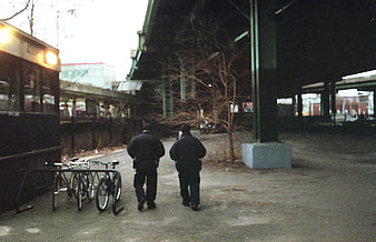 Two men walking away under urban bridge with bicycles