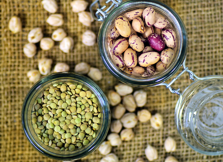 Top view of dried legumes in glass jars on burlap