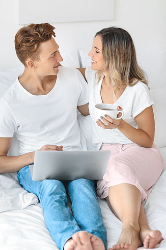 Happy young couple using laptop in bed with coffee