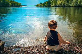 Toddler Boy Sitting by Lake Shore in Summer