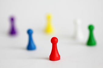 Red game pawn leading colorful blurred pieces on white background