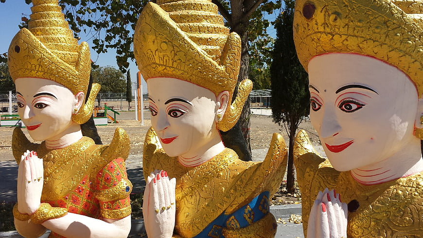 Three golden Cambodian statues in prayer pose outdoors