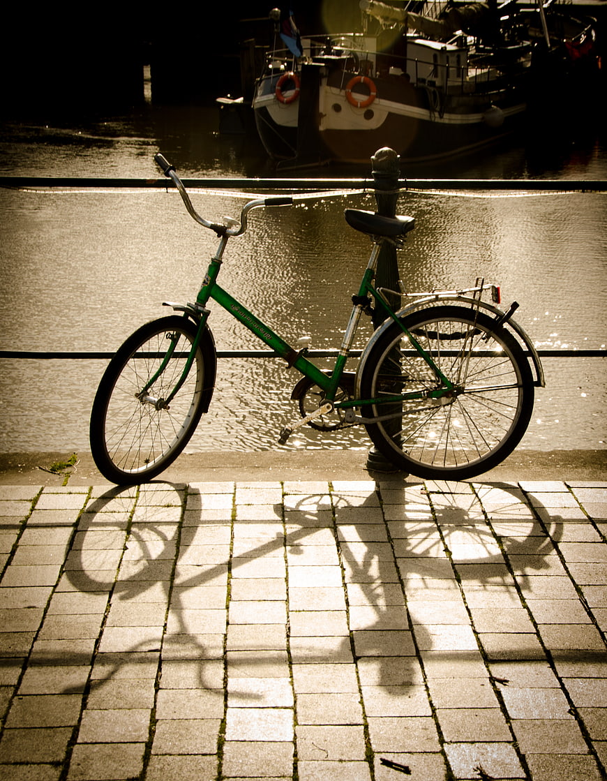 Green Bicycle Parked by Canal with Strong Shadows