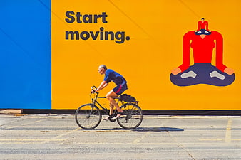 Senior cyclist riding past vibrant yellow and blue urban advertising wall
