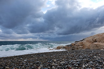 Dramatic stormy sky over rocky pebble beach with crashing waves