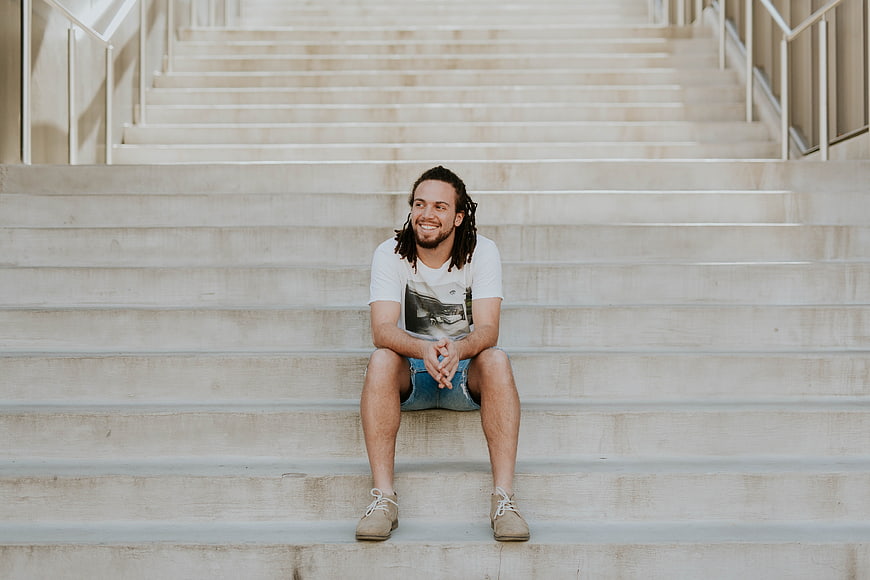 Happy man with dreadlocks sitting on concrete stairs