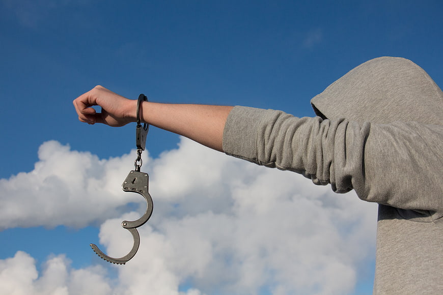Person in Hoodie with Open Handcuffs Against Blue Sky