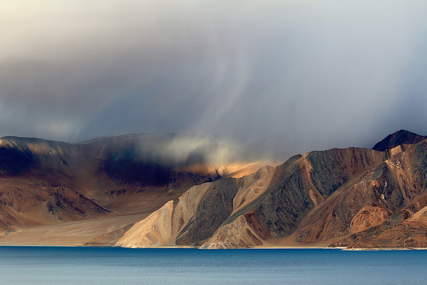 Dramatic storm clouds over arid mountains and blue lake
