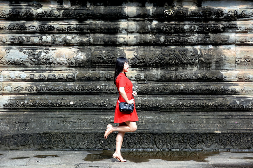 Woman in Red Dress Walking Past Ancient Stone Wall