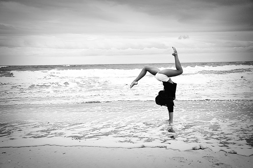 Woman performing a one-handed handstand on a black and white beach