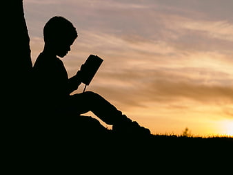 Silhouette of Boy Reading Book at Sunset