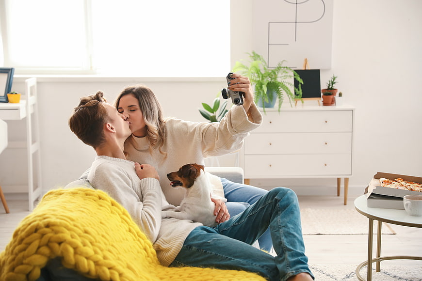 Couple taking selfie with dog and vintage camera on sofa