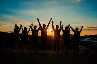 Group of friends silhouetted with raised hands at sunrise