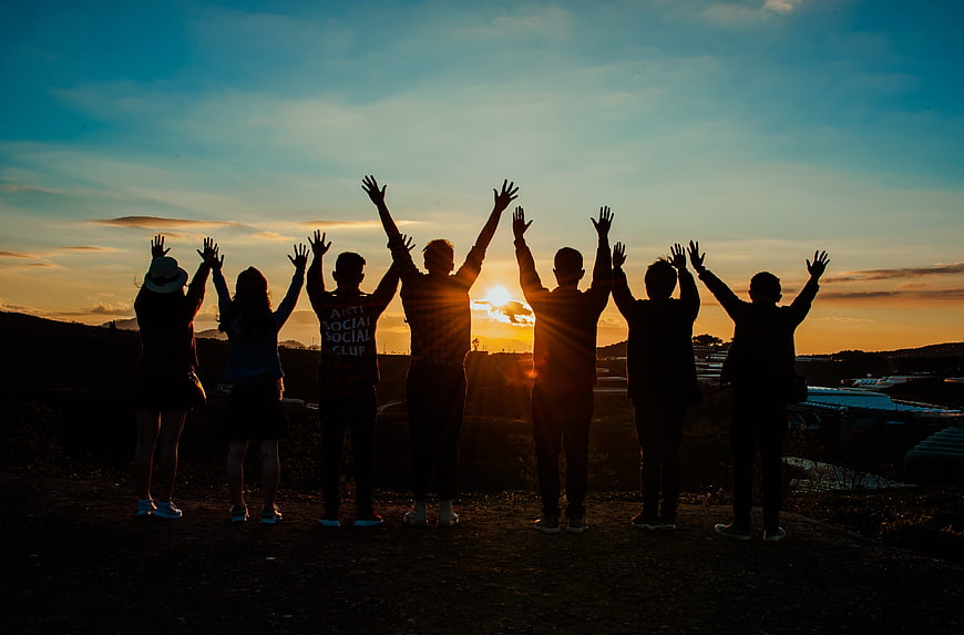 Group of friends silhouetted with raised hands at sunrise