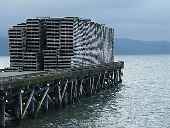 Stacks of wooden pallets on a weathered pier over calm water