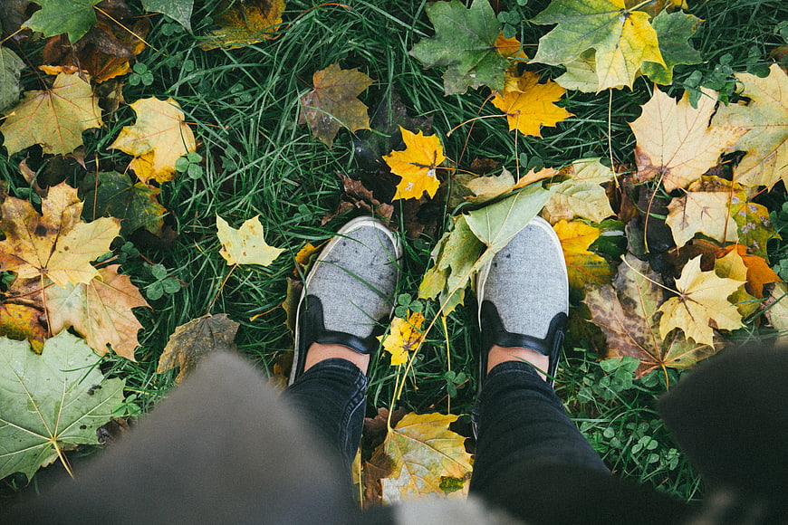 First-person view of feet in grey slip-on shoes on autumn leaves