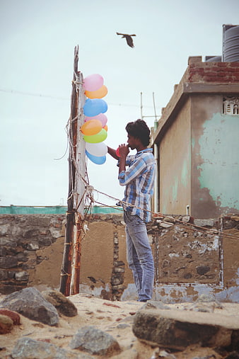 Man Tying Colorful Balloons to Wooden Pole on Rooftop