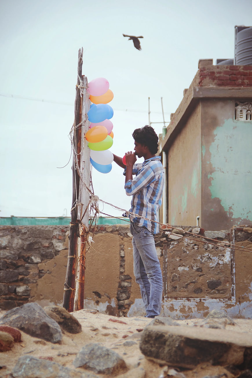 Man Tying Colorful Balloons to Wooden Pole on Rooftop