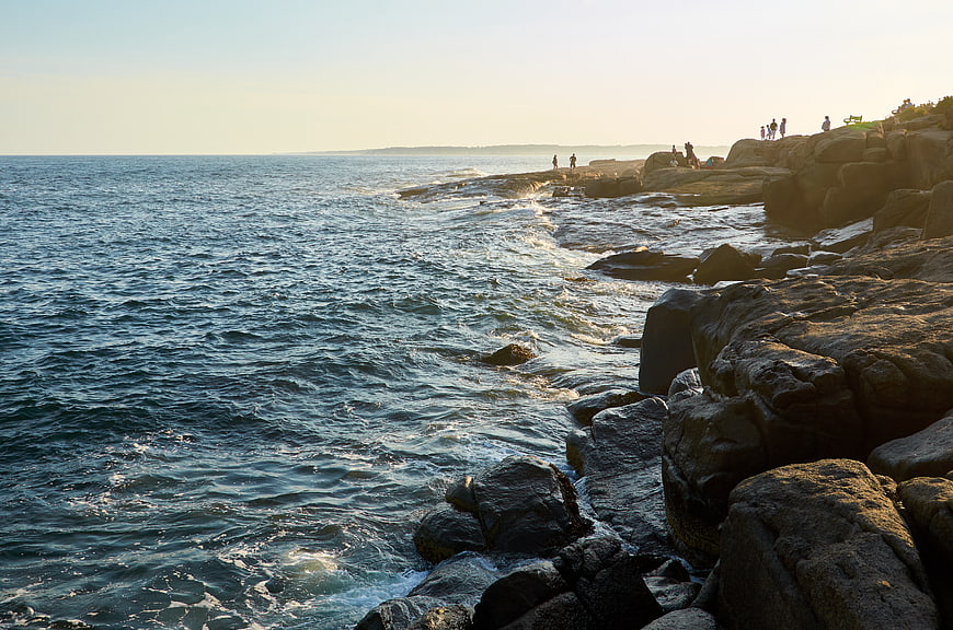 Sunlit Rocky Coastline with Ocean Waves and People