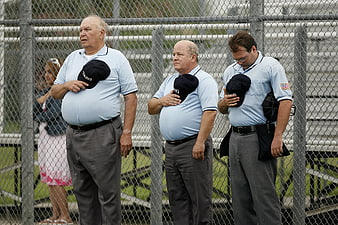 Three Umpires Standing At Chain-Link Fence During Softball Game