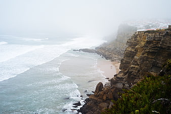 Foggy coastal cliffs overlooking a sandy beach and ocean waves