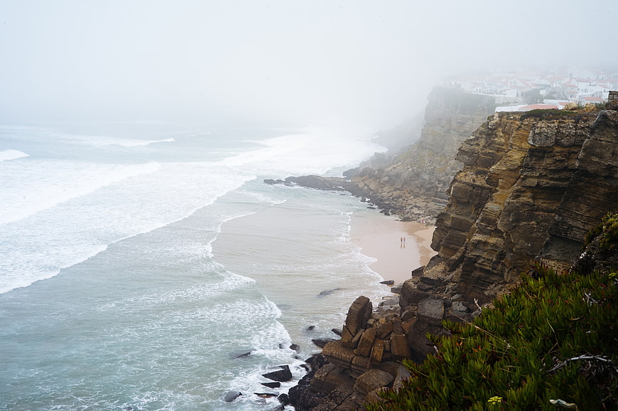 Foggy coastal cliffs overlooking a sandy beach and ocean waves