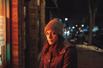 Woman in winter coat and beanie on city street at night