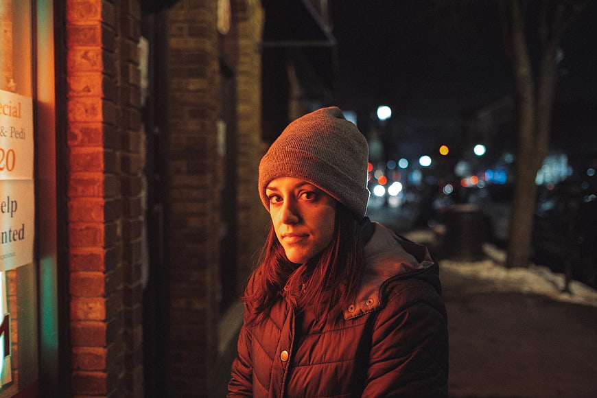 Woman in winter coat and beanie on city street at night