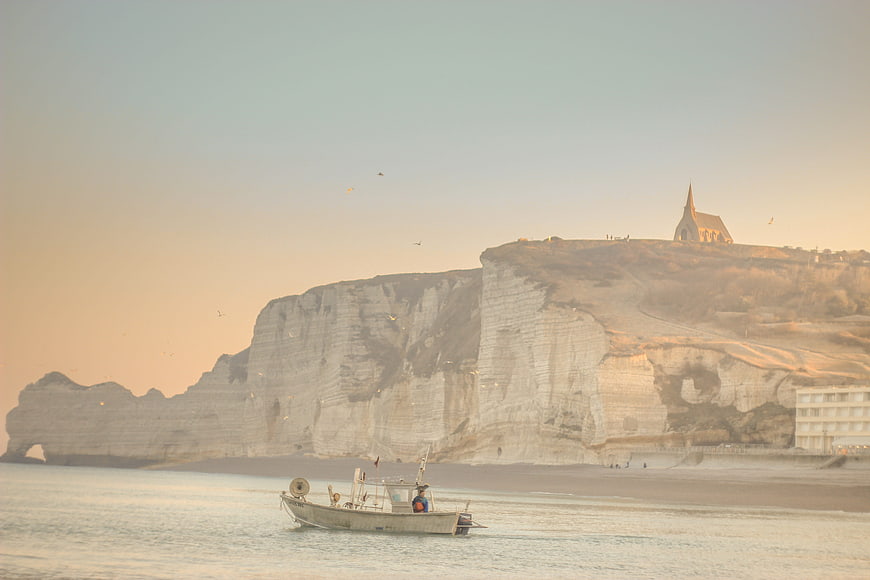 Fishing boat near Etretat cliffs and church at sunrise