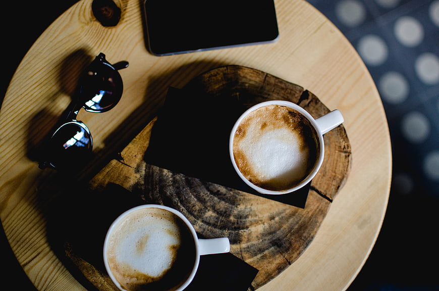 Top view of two cappuccinos on a wooden table with sunglasses and smartphone