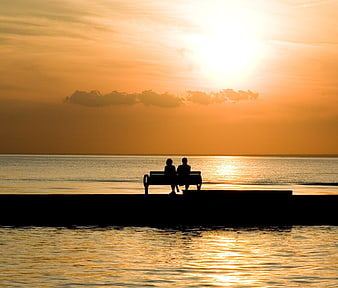 Silhouette of couple sitting on bench at sunset by the water