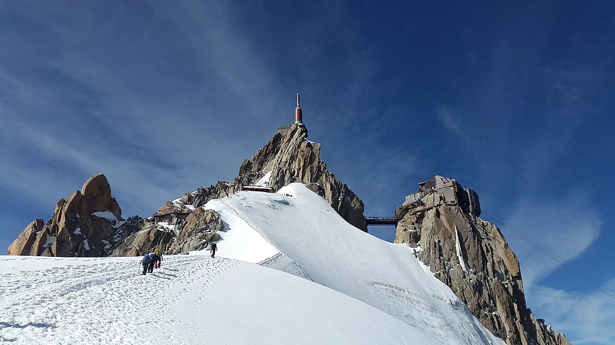 Hikers on Snowy Mountain Slope with Rocky Peak and Blue Sky