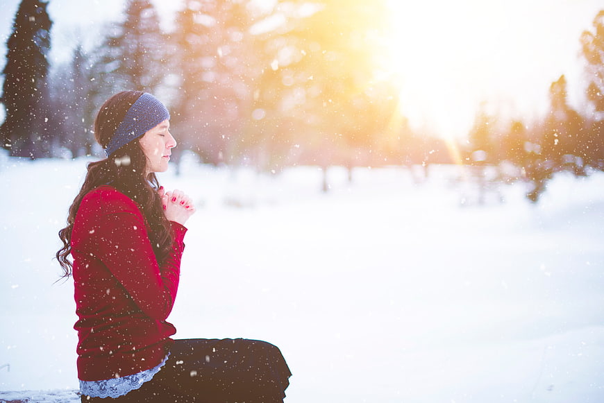 Woman Praying in Snowy Winter Landscape with Sunlight