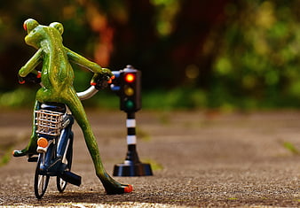 Green frog figurine riding bicycle at red traffic light