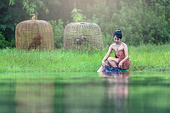 Young woman doing laundry in a river with woven baskets in the background