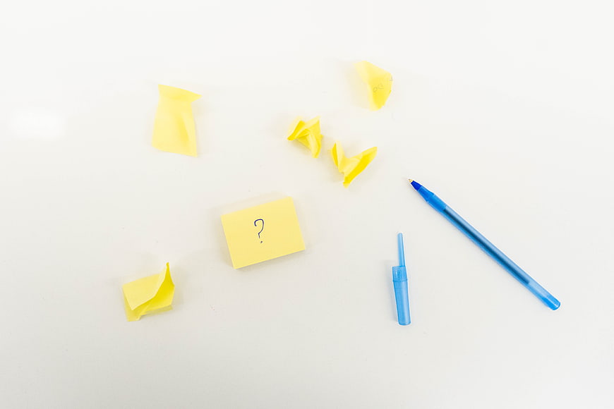 Yellow sticky notes with question mark and blue pen on white background