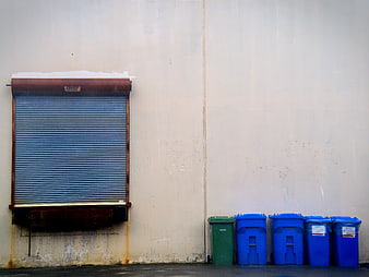 Blue and green recycling bins against a weathered urban wall